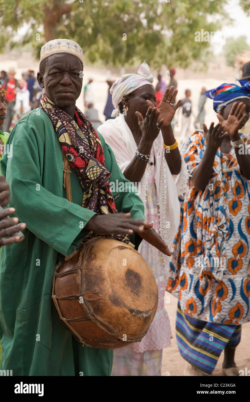 Un homme joue un tambour calebasse que les femmes La danse et applaudir durant la fête du cheval en FECHIBA Barani, Burkina Faso Banque D'Images