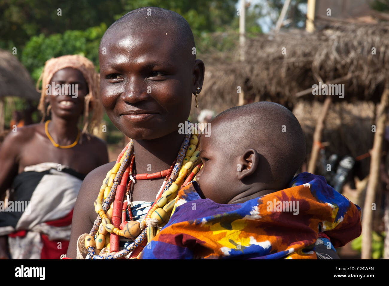 Une prêtresse animiste avec une tête rasée tient son bébé dans un marché de plein air au Togo, en Afrique de l'Ouest. Banque D'Images