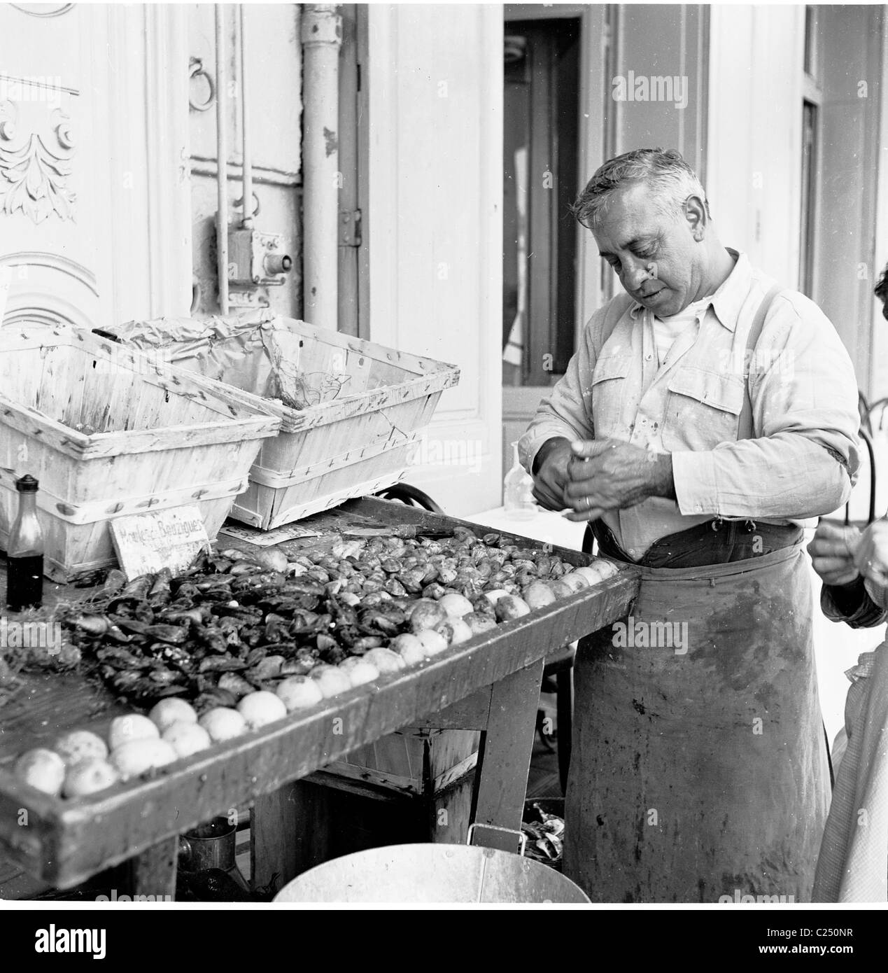 1950s, photo historique par J Allan Cash d'un commerçant français ouvrant des obus sur sa cale à poissons du vieux port de Marseille, France. Banque D'Images