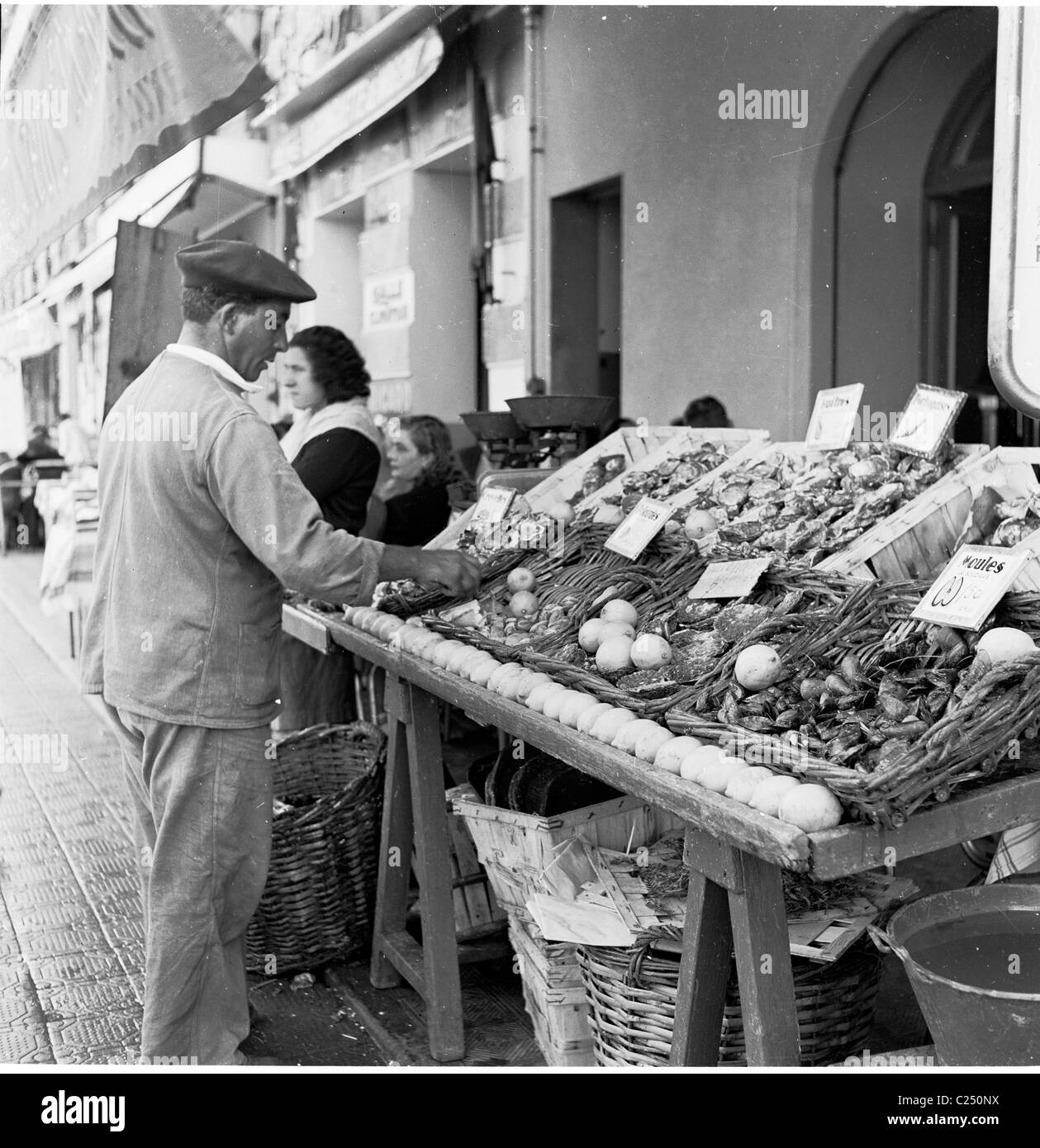 France,1950. Négociant mâle avec berry contrôle de l'écran de poissons sur son stand au vieux port à Marseille. Banque D'Images