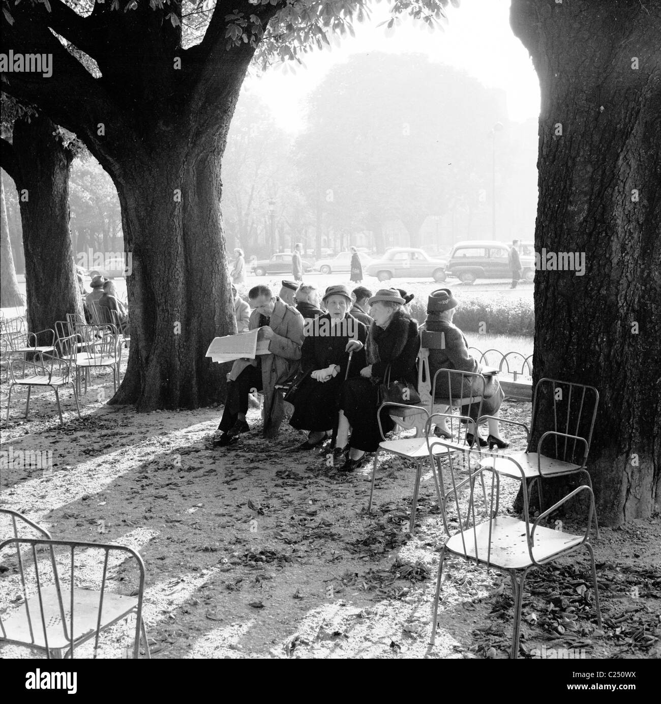 France,1950. L'hiver et en extérieur dans un cadre, un homme lit son journal avec d'autres parisiens assis ensemble sur un banc à Paris. Banque D'Images