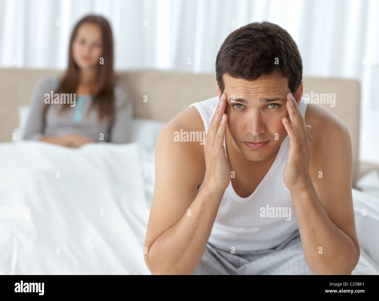 Homme fatigué d'avoir un mal de tête assis sur le lit avec sa petite amie Banque D'Images