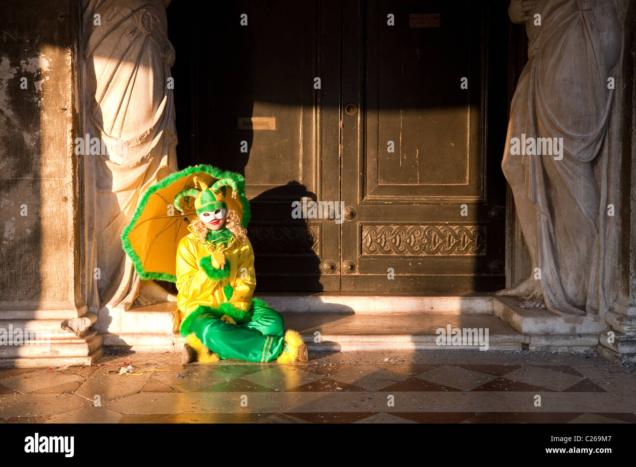 Une jeune femme en costume clown assis dans une porte, la place St Marc, le carnaval, Venise, Italie Banque D'Images