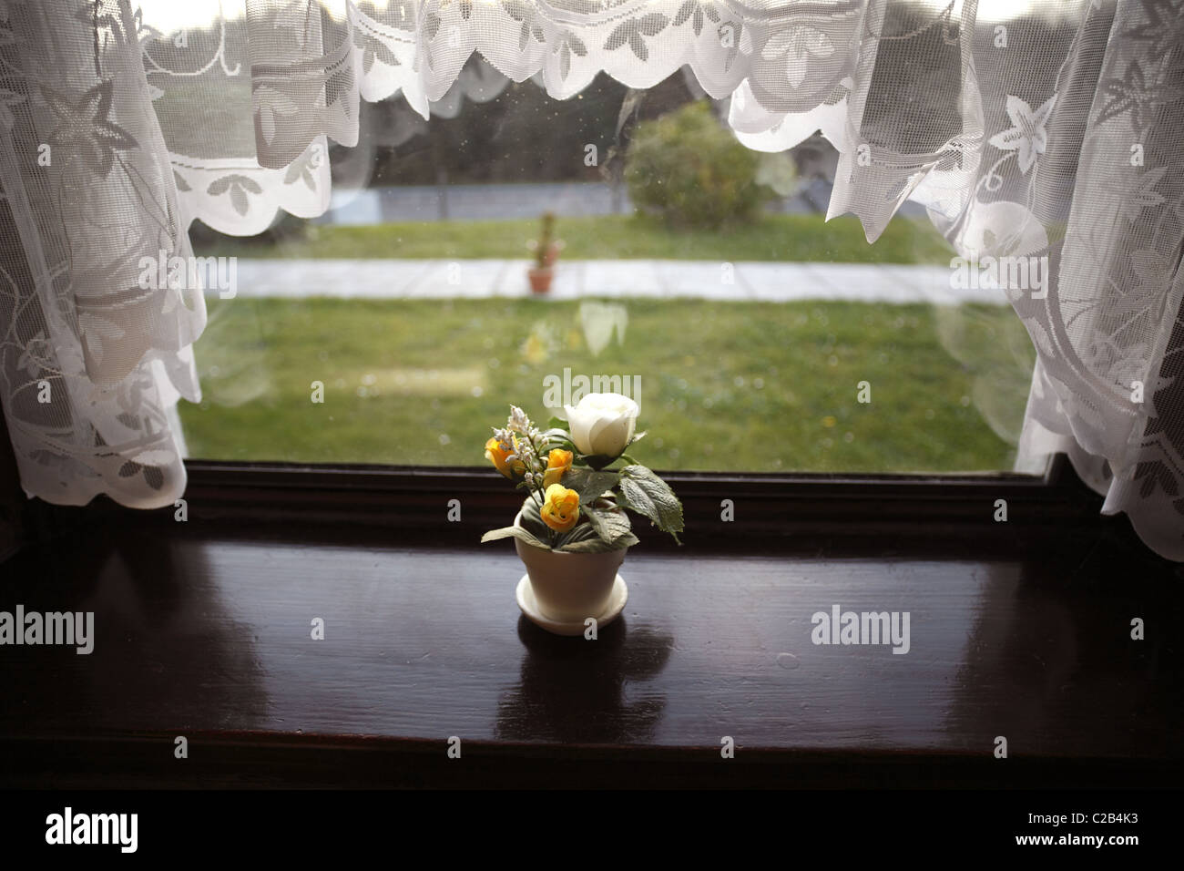 Des fleurs en plastique sur le rebord de fenêtre encadrée de rideaux net. Banque D'Images