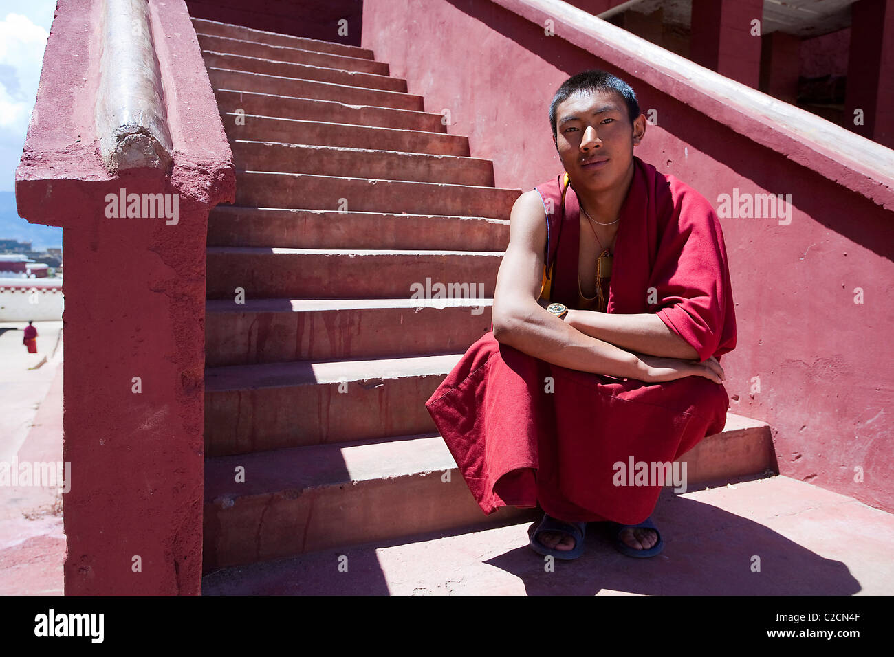 Jeune moine bouddhiste s'accroupit en face de certaines étapes de sa robe le Tibet/Chine Banque D'Images