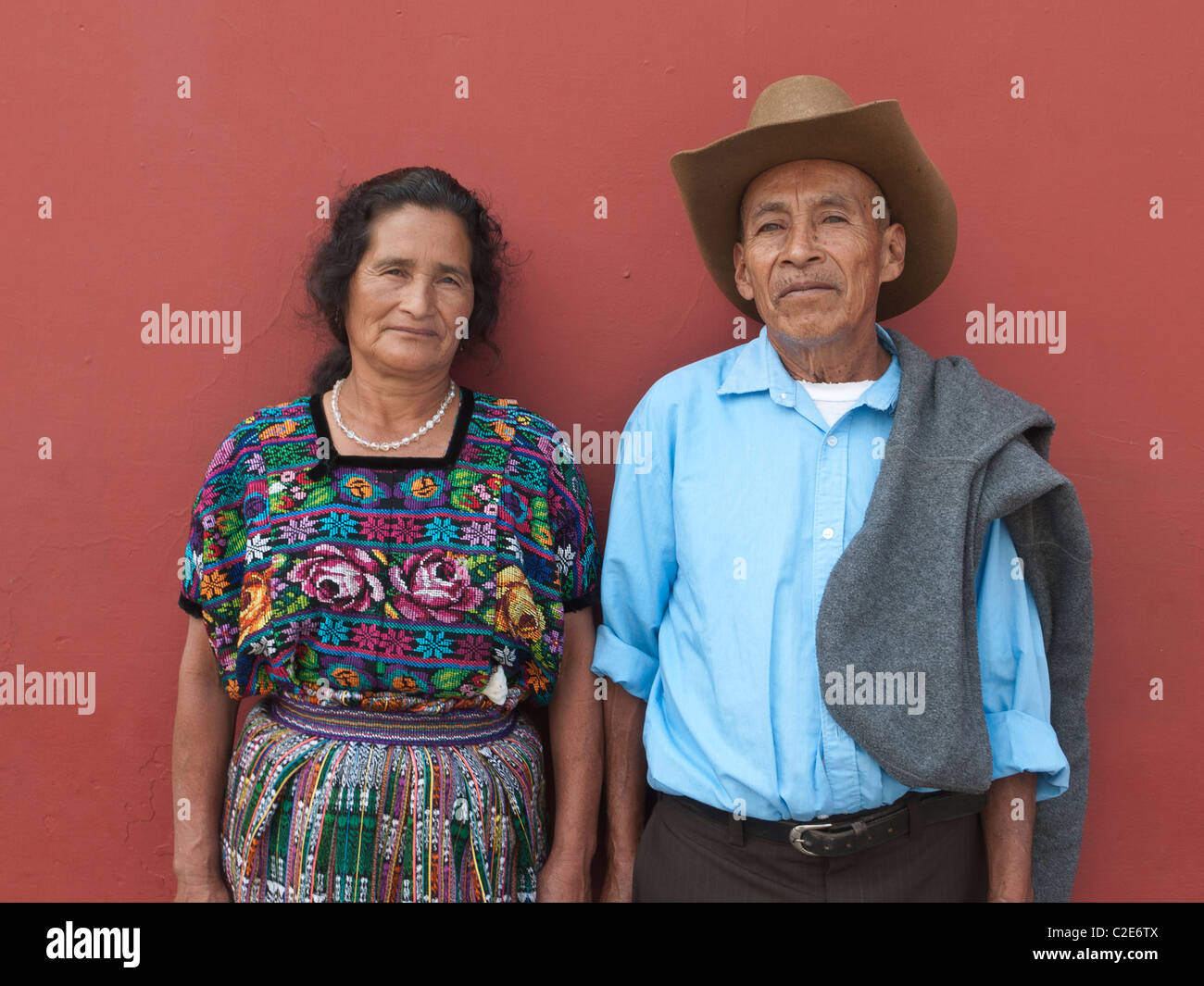 Un vieux couple marié guatémaltèque se tenir en face d'un mur de couleur terre cuite profonde en costume traditionnel à l'avant. Banque D'Images