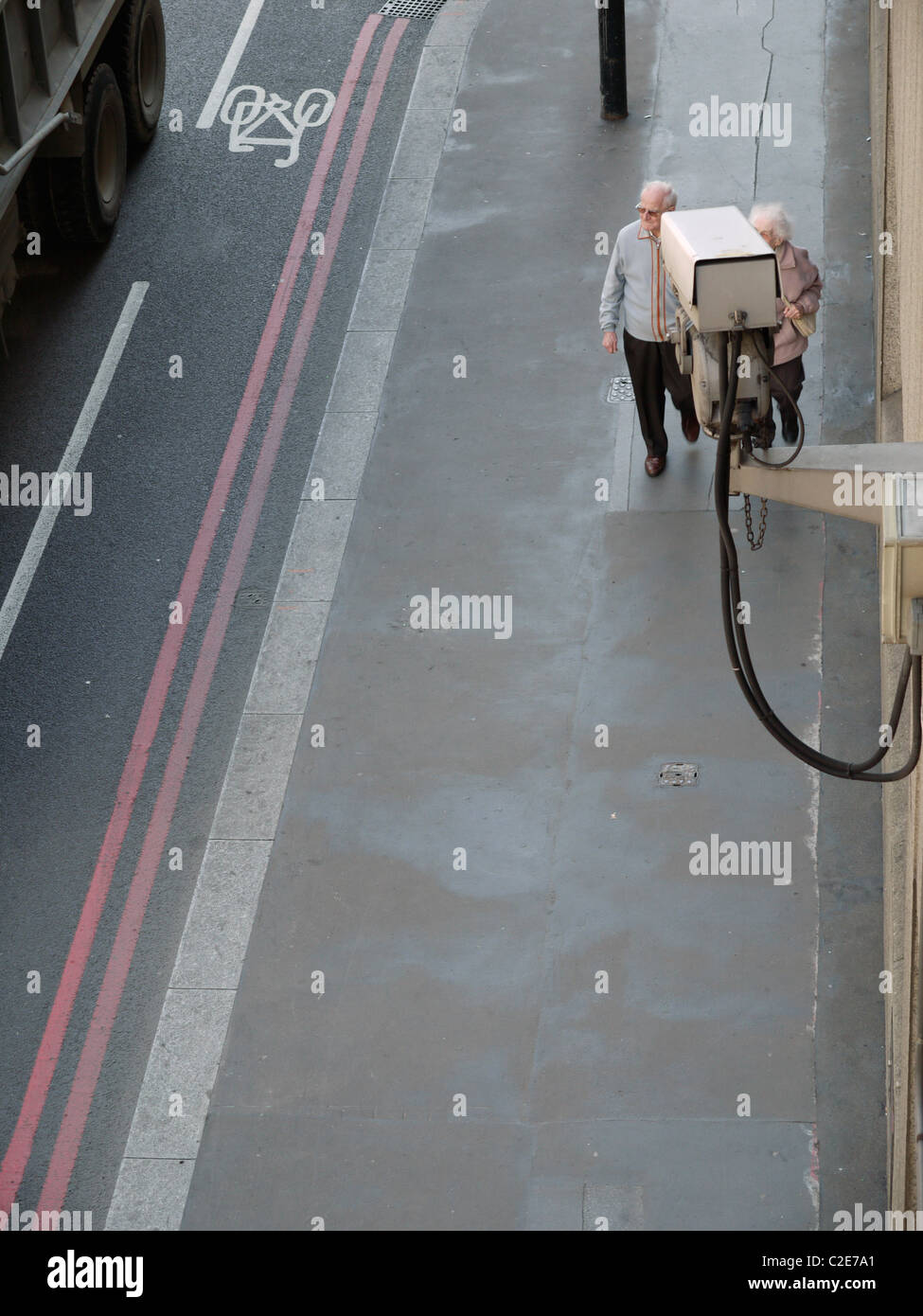 Vidéosurveillance Caméra montée sur le bâtiment, avec vieux couple walking passé Banque D'Images
