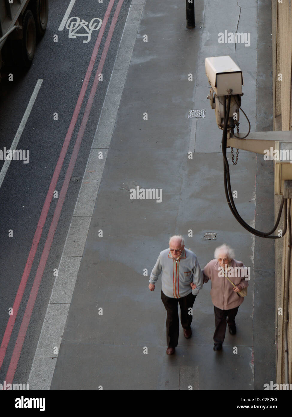 Vidéosurveillance Caméra montée sur le bâtiment, avec vieux couple walking passé Banque D'Images