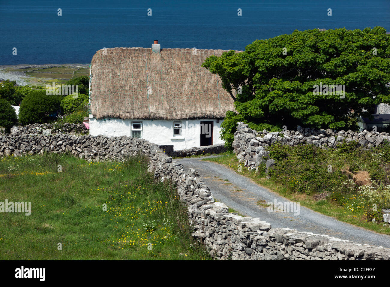 Chaumière blanchis à avec murs en pierre sèche et la baie de Galway derrière Banque D'Images