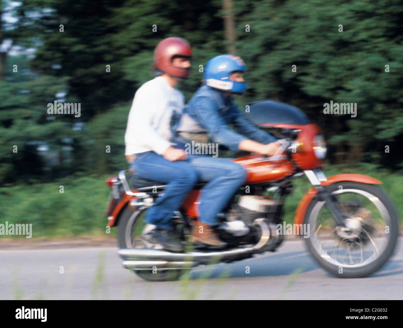 Années 70, les gens, la circulation, la sécurité routière, de la jeunesse, deux jeunes gens assis sur une moto roulant sur une route de campagne, conducteur, passager, leurs casques, floues, brouillées, âgés de 16 à 23 ans Banque D'Images