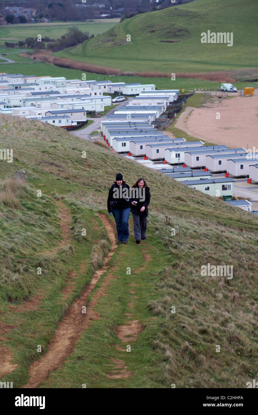 Deux femmes avec des caméras marchant en haut de la colline avec garage, site de caravane derrière à West Bay, Dorset Royaume-Uni en janvier - caravanes statiques mobile homes Banque D'Images