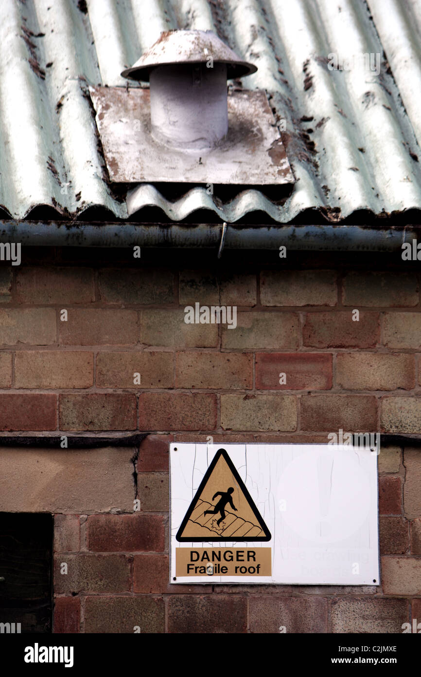 Un panneau d'avertissement disant Danger : toit fragile et montrant une toiture en métal qui a besoin de réparations avec un canal Banque D'Images