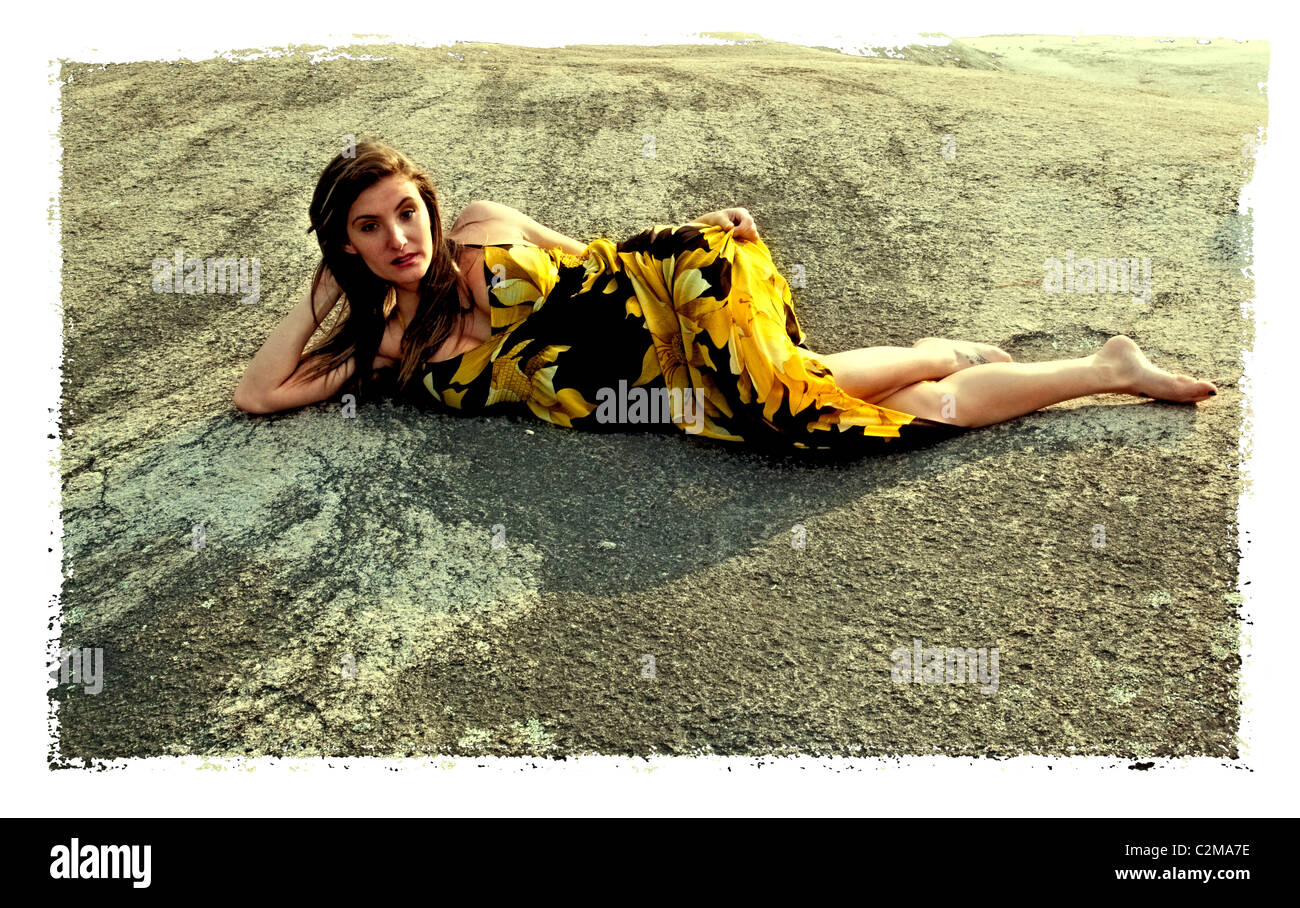 Jolie femme en robe jaune et noire à l'extérieur pose sur la roche, avec un contact visuel Banque D'Images