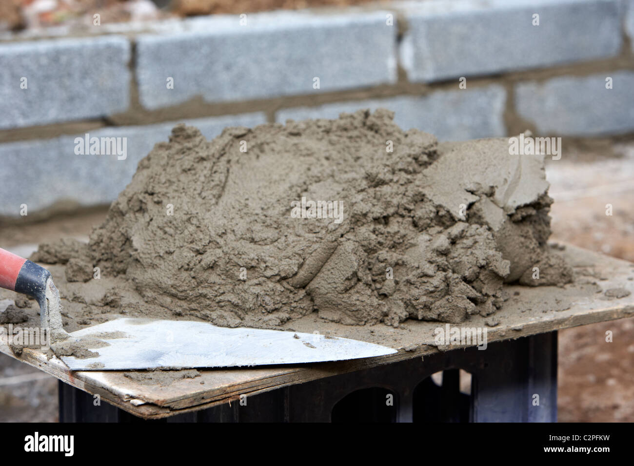 La truelle et le mortier de maçonnerie empilés sur une planche en bois prêt pour la construction d'un mur de soutènement en bloc au Royaume-Uni Banque D'Images