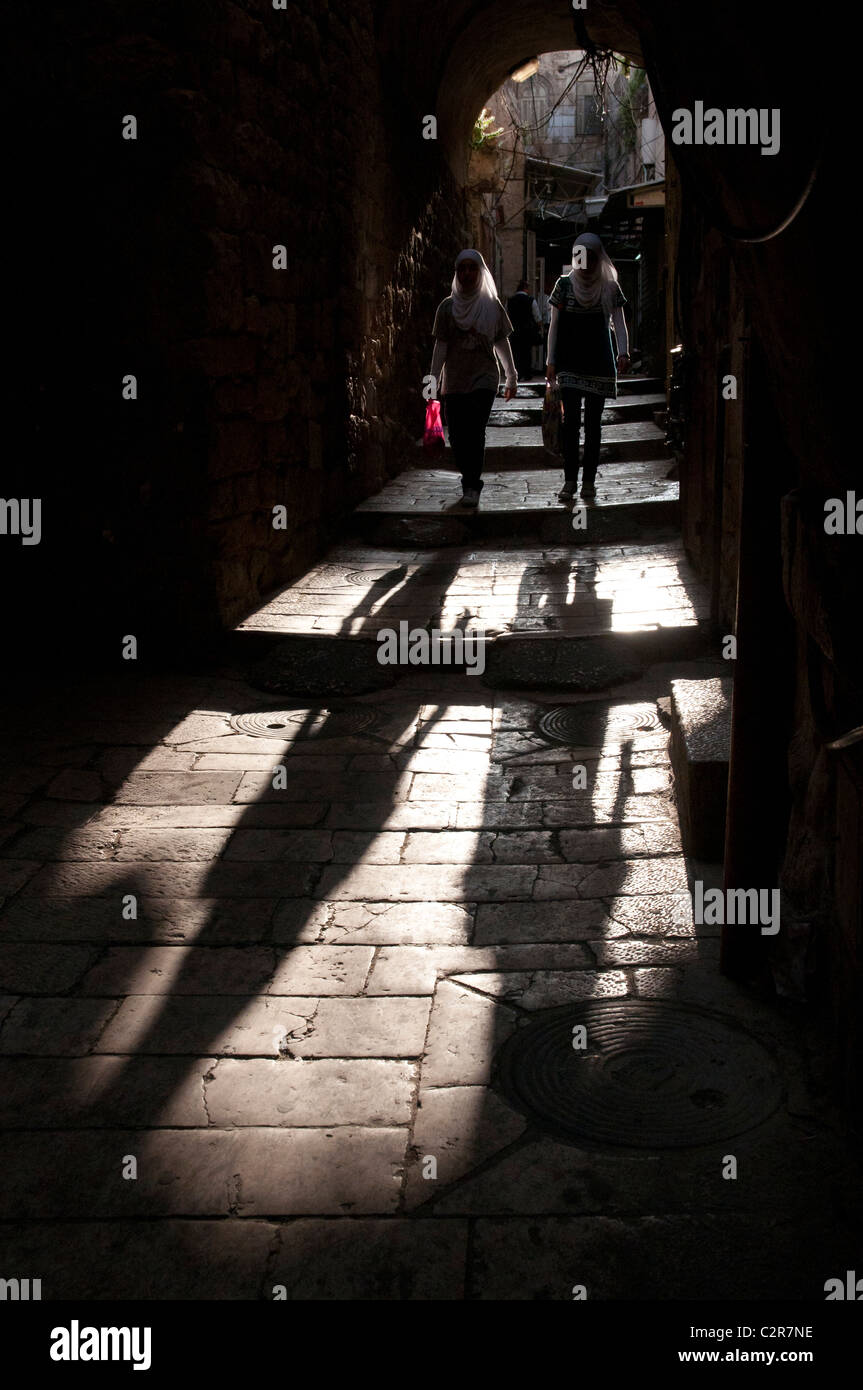 Deux femmes palestiniennes marche à travers une arche dans une rue de la vieille ville de Jérusalem avec des ombres. Banque D'Images