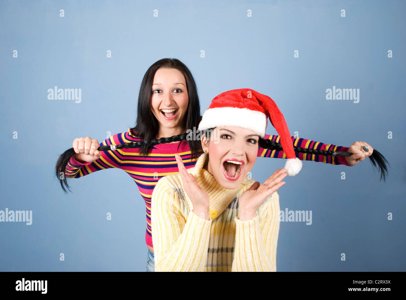 Un Funny Girl with Santa hat d'avoir ses tresses tiré par son amie et les deux rient et de crier et de s'amuser Banque D'Images