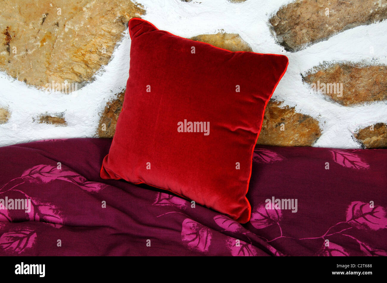 Coussin velours rouge appuyé contre un mur de pierre. Banque D'Images