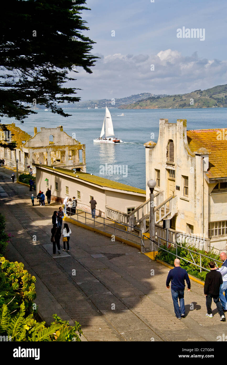 Les touristes passent devant la détérioration des bâtiments de stockage à l'ancienne prison fédérale d'Alcatraz à San Francisco, CA. Remarque voilier Banque D'Images