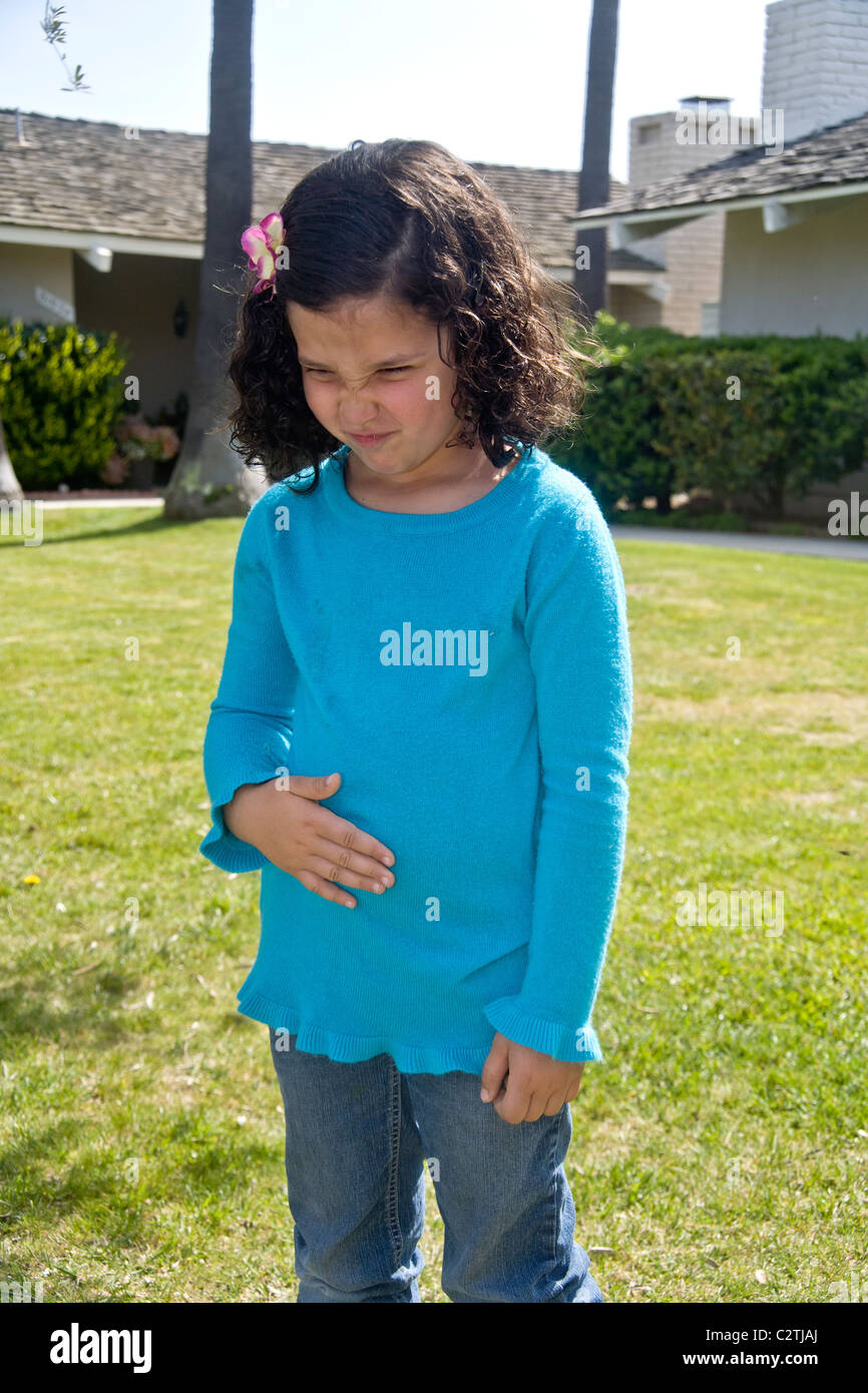 Un enfant de cinq ans Egyptian-American fille grimace de douleur d'un estomac à l'extérieur dans Laguna Niguel, CA. Banque D'Images