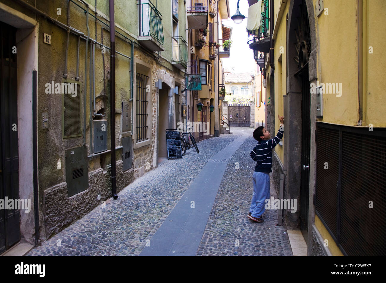 Jeune garçon sonne sur une sonnette dans une ruelle dans la ville d'ISEO LAC D'Iseo Italie Banque D'Images