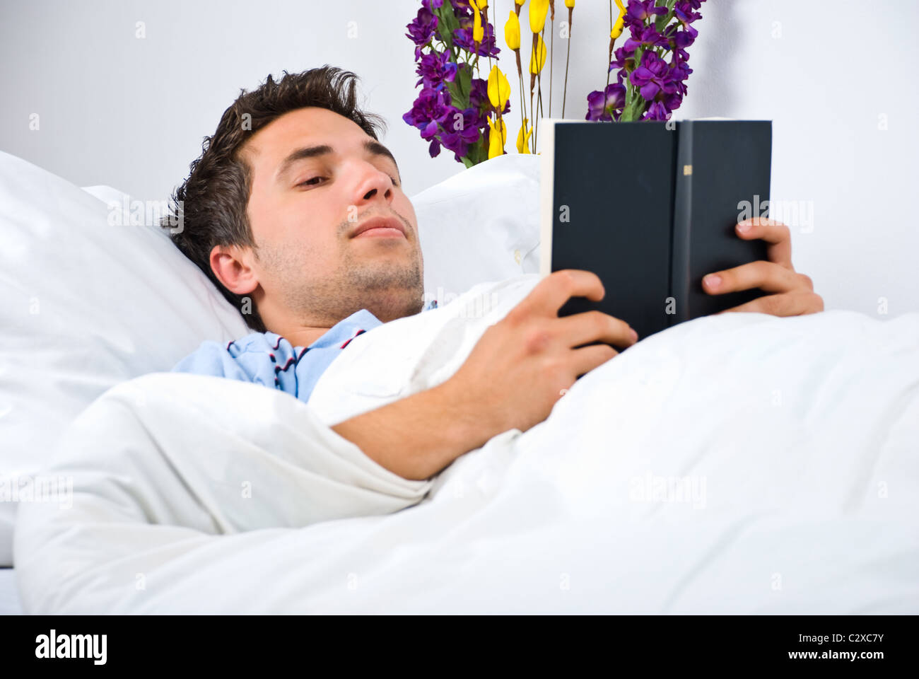 Jeune homme lire un livre sur le lit avant de dormir Banque D'Images