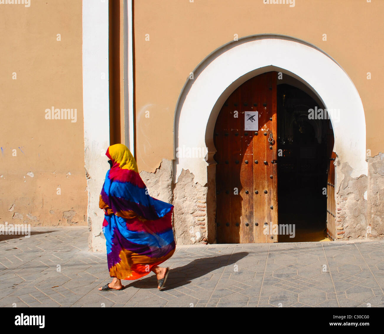 Femme en découlant, colorés, jellaba en passant devant une porte ouverte à Taroudant, Maroc Banque D'Images