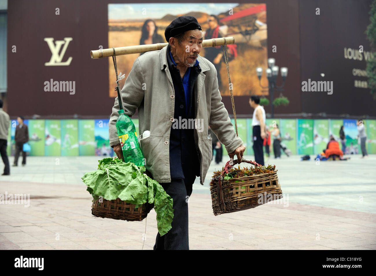 Un vieil homme vendant des légumes en face de Louis Vuitton billboard au centre-ville de Chongqing, Chine. 22-Apr-2011 Banque D'Images