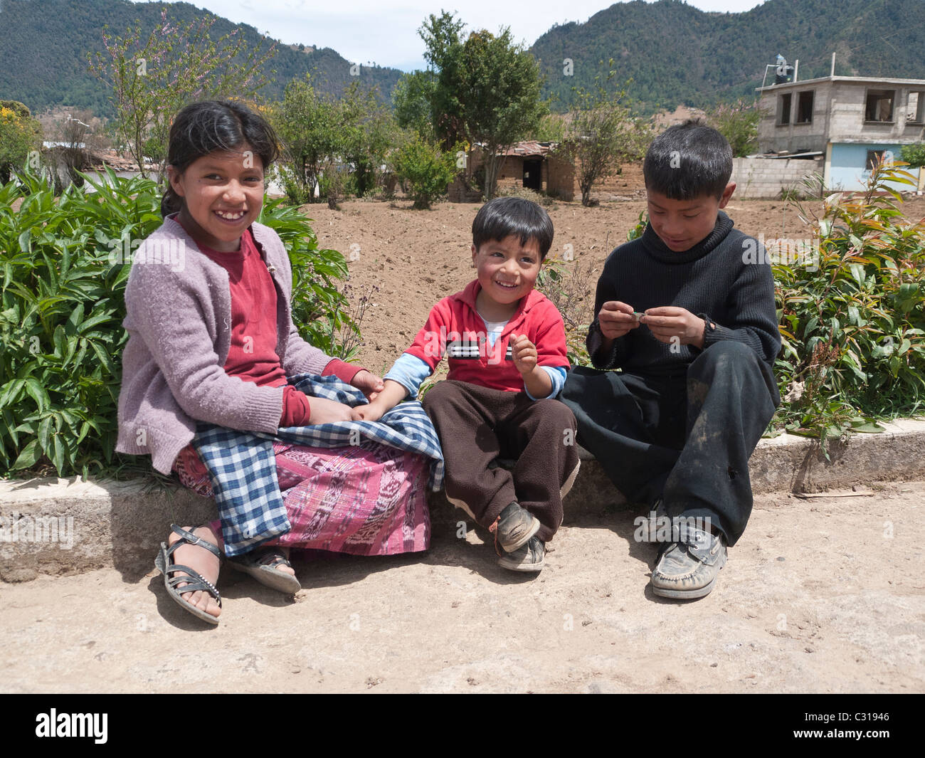 Trois jeunes enfants guatémaltèques jouer sur le côté d'une route rurale près de leur maison à Totonicapan, Guatemala. Banque D'Images