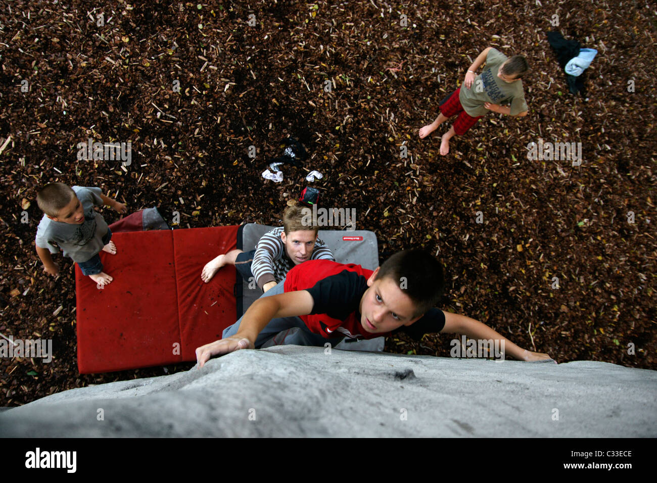 Jeune garçon enfant escalade bouldering pendaison route difficile à boulder rocher au-dessus de coffre crashpad high angle shot Banque D'Images