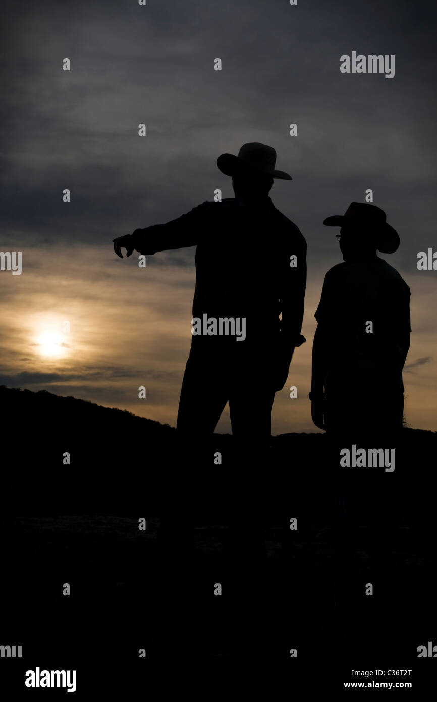Père Cowboy est fièrement montrant la terre à son fils au coucher du soleil. Banque D'Images