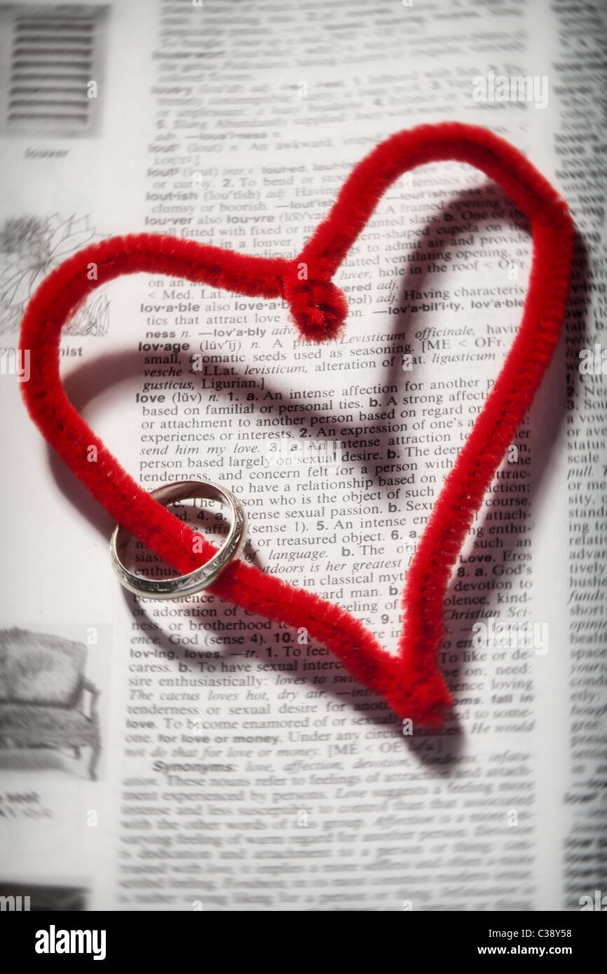 Un cœur rouge avec une bande de mariage d'argent enroulé sur elle avec le cœur entourant la définition de l'amour dans le dictionnaire Banque D'Images