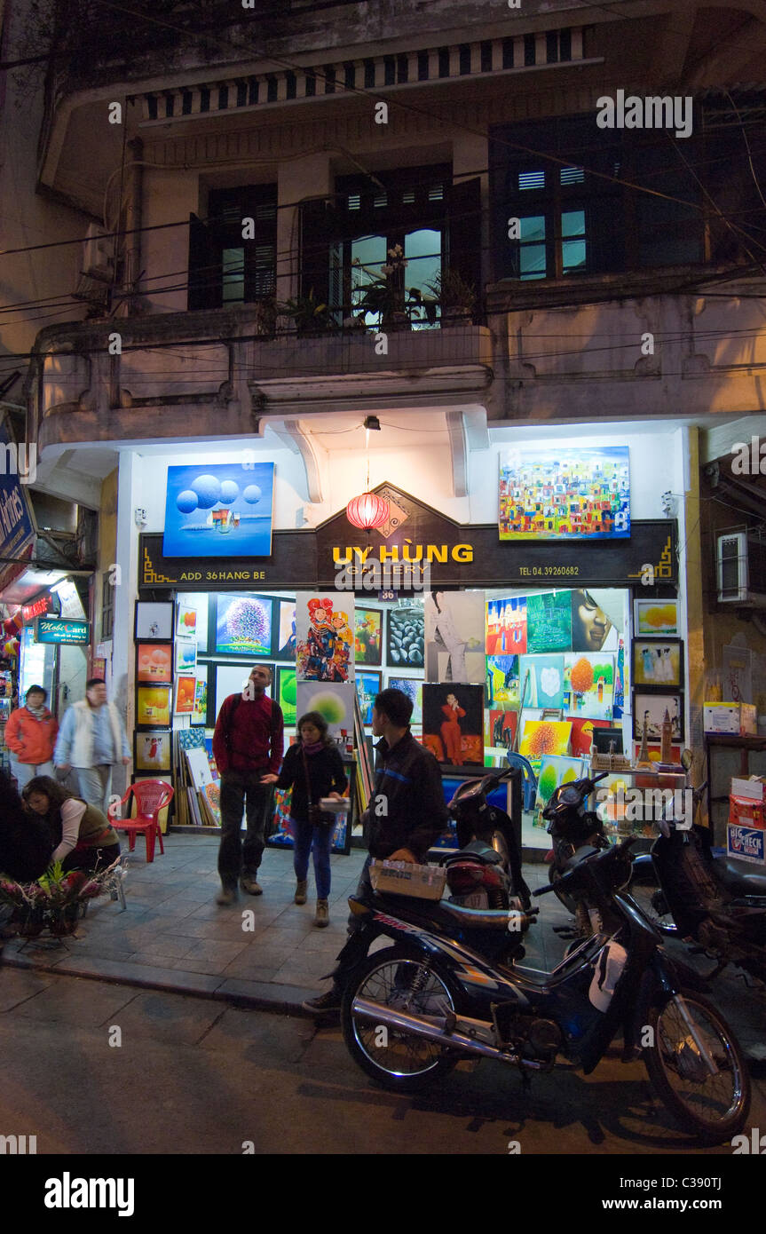 La nuit verticale d'un point de vue extérieur les touristes une galerie vente de grandes toiles à Hang Be Street dans le vieux quartier de Hanoi. Banque D'Images