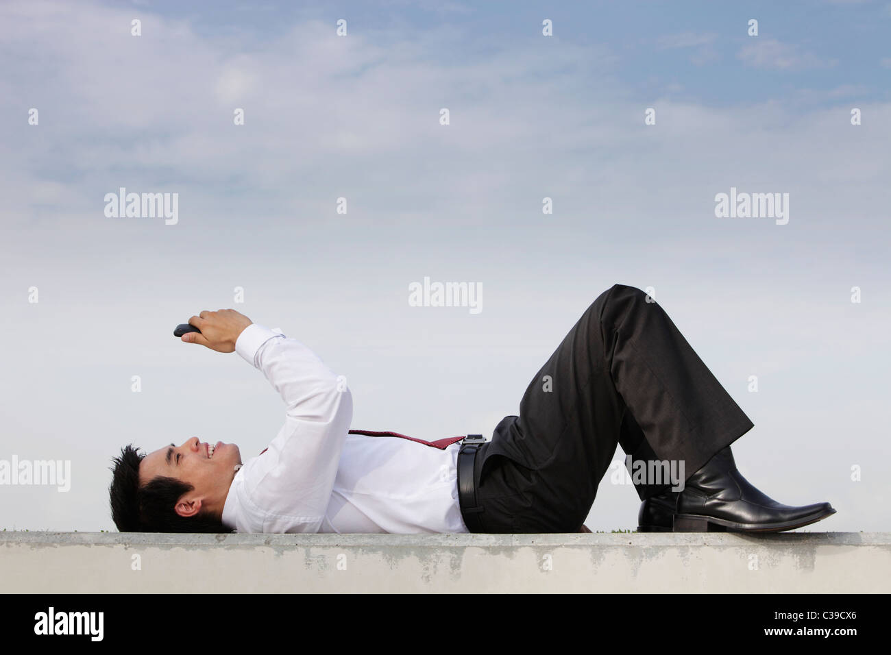 Man in suit portant sur le sol regardant phone smiling Banque D'Images