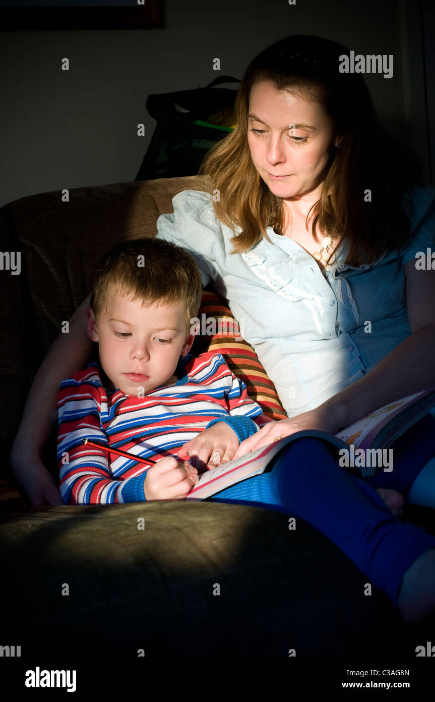 Mère et son jeune fils faire leurs devoirs dans un arbre de lumière sur un divan, spotlight, stripe, pyjamas, PJ's, maman, fils, garçon, enfant, Banque D'Images
