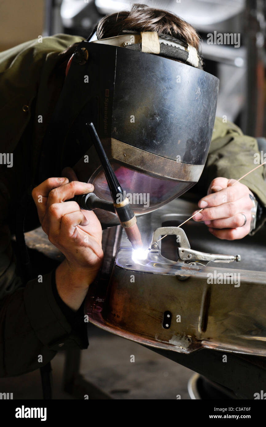 Un travailleur qualifié au métal de travail des métaux, en utilisant la méthode de soudage TIG pour effectuer une réparation sur un VW camping-porte. Banque D'Images