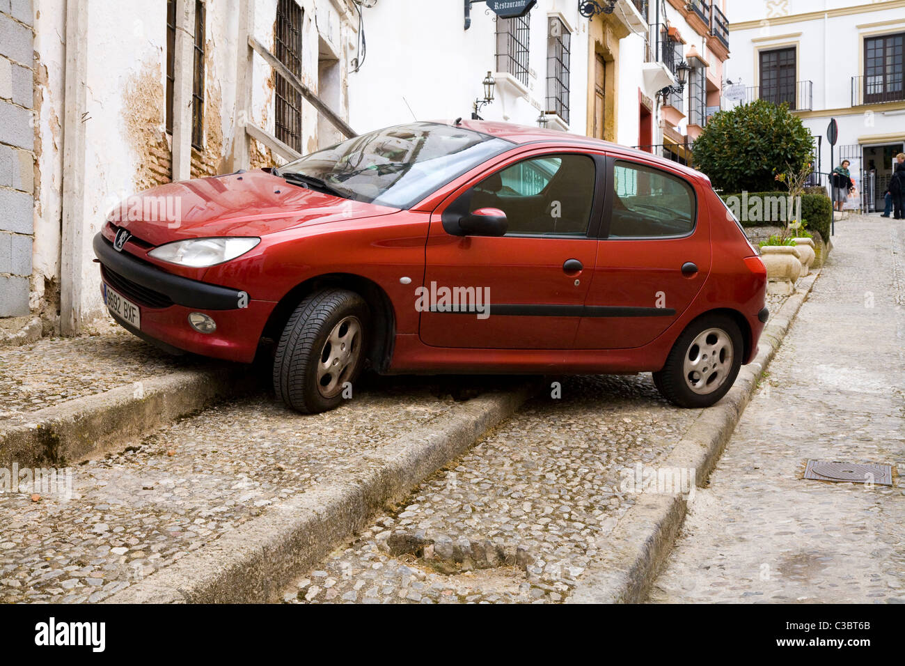 Une Peugeot 206 voiture garée sur le trottoir en espagnol traditionnel typique route pavée / Street dans la ville blanche de Ronda, Espagne. Banque D'Images