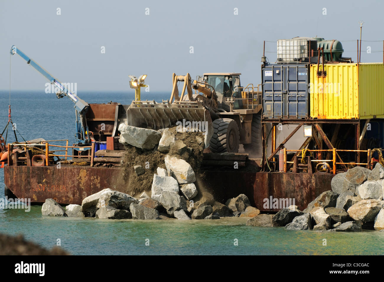 Les entrepreneurs le déchargement d'une barge au large des rochers le renforcement de la défense à la mer sur la baie de Cardigan Borth côte de l'ouest du pays de Galles UK Banque D'Images