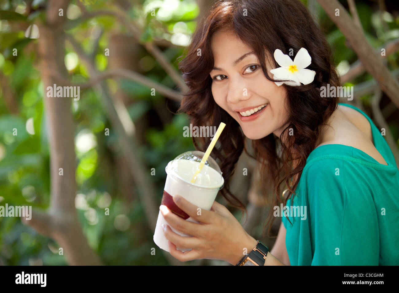 Smiling asian femme thaïlandaise de boire du jus de fruits avec une fleur dans les cheveux Banque D'Images