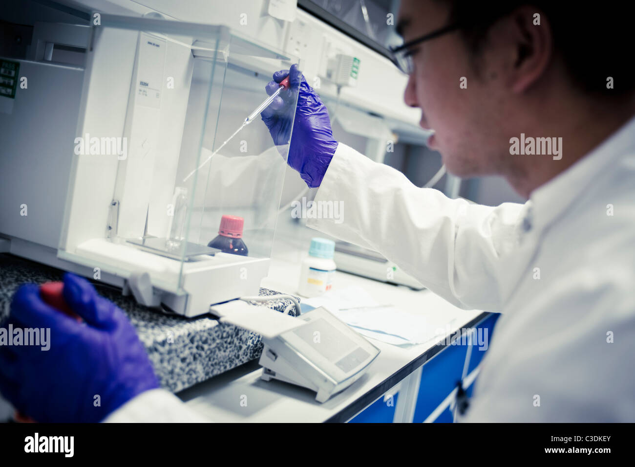Asian male scientist en sarrau blanc et violet gants avec pipette in lab à des échelles Banque D'Images