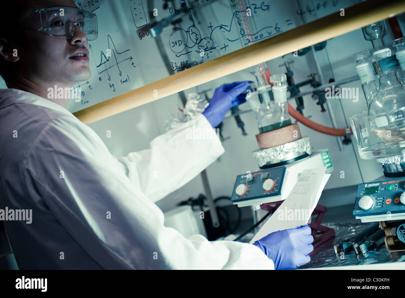 Asian male scientist en manteau blanc et violet lunettes gants à la hotte de laboratoire en examinant de près l'équipement de test tube Banque D'Images