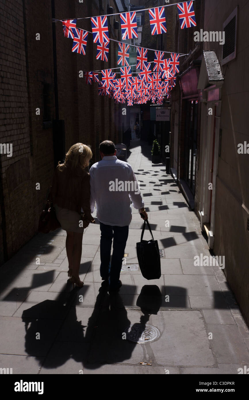 Couple à pied ci-dessous British Union Jack Drapeaux montés ensemble dans une ruelle de Londres, à proximité de Bond Street. Banque D'Images