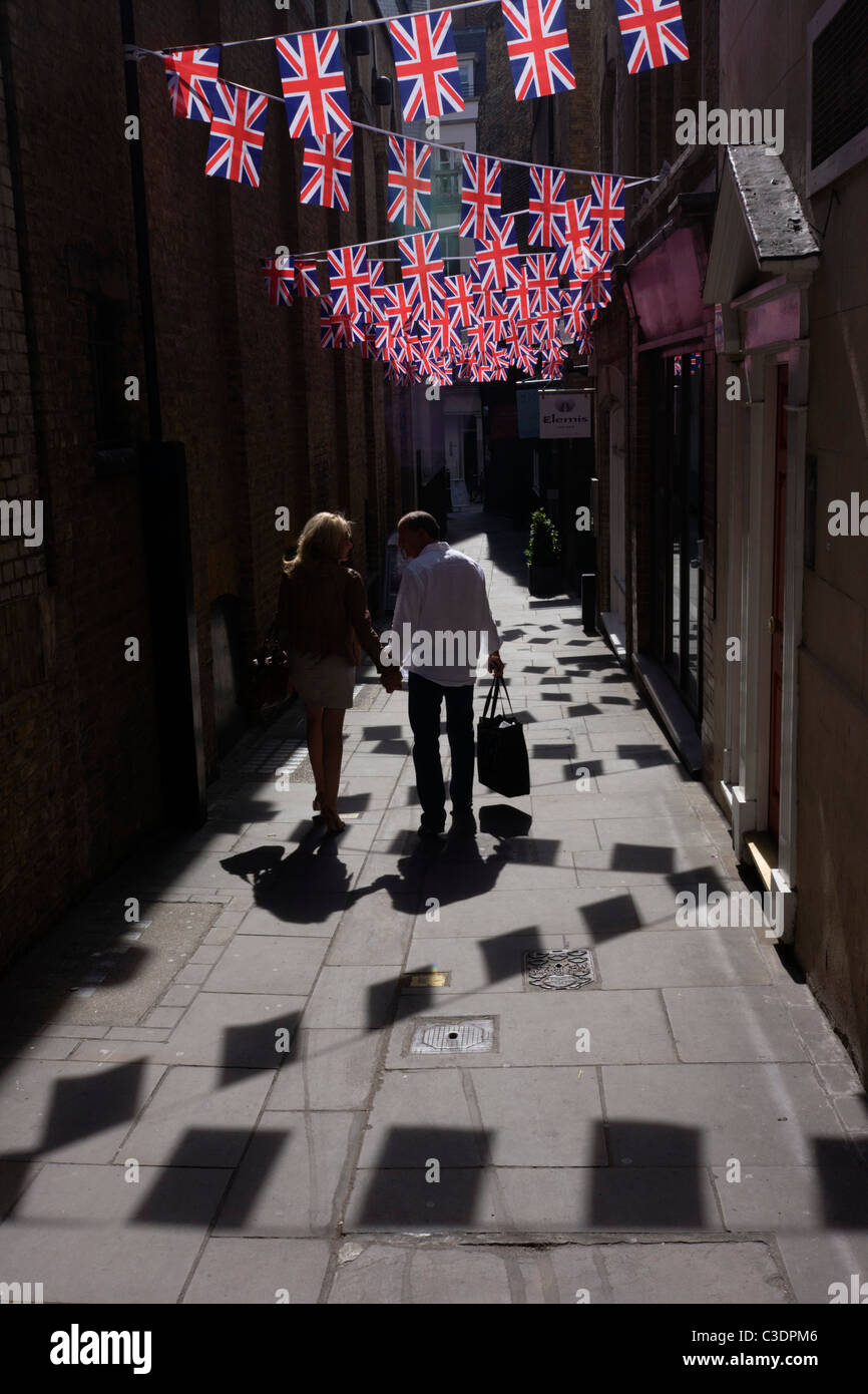 Couple à pied ci-dessous British Union Jack Drapeaux montés ensemble dans une ruelle de Londres, à proximité de Bond Street. Banque D'Images