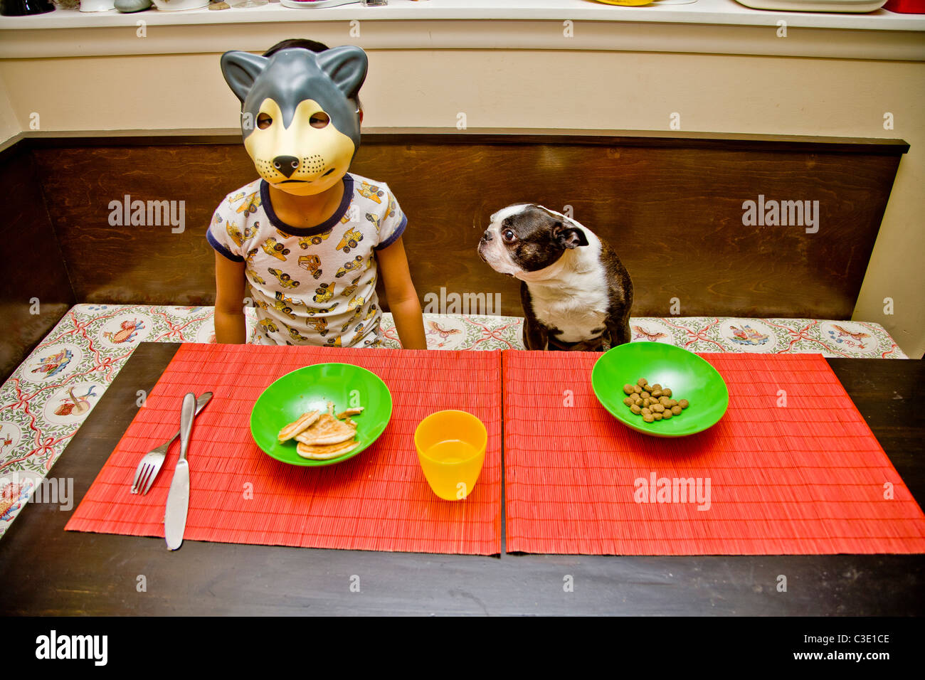 Enfant dans le masque de loup à la table avec chien d'animal de compagnie Banque D'Images