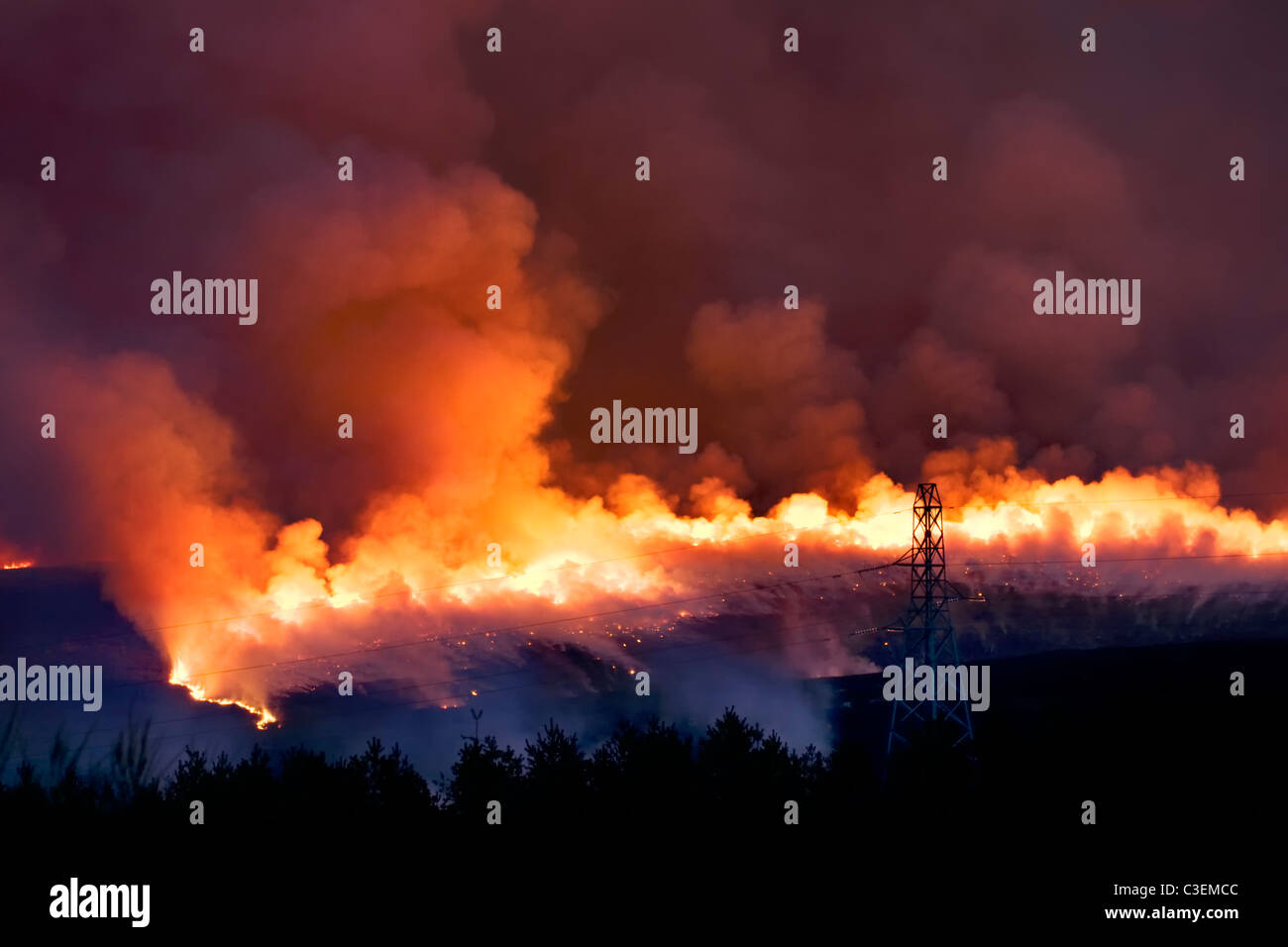 Un feu de broussailles intense sur les collines près de l'A836 entre Lairg et Bonar Bridge en Ecosse prises au crépuscule avec pylône en premier plan Banque D'Images