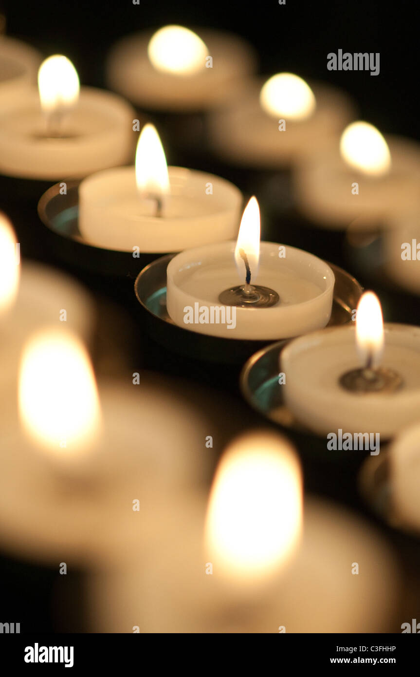 Trois rangées de bougies votives brûlant avec un fond noir Banque D'Images