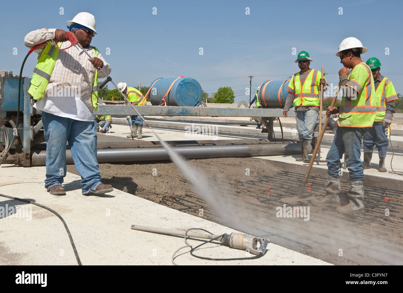 Autoroute de l'homme hispanique au cours de l'eau sprays travailleur le béton fraîchement coulé pour assurer la bonne température Banque D'Images