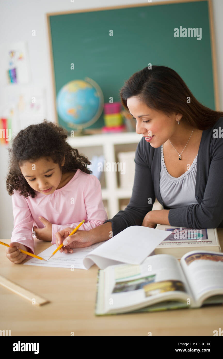 Girl (6-7) with female teacher sitting at desk in classroom Banque D'Images