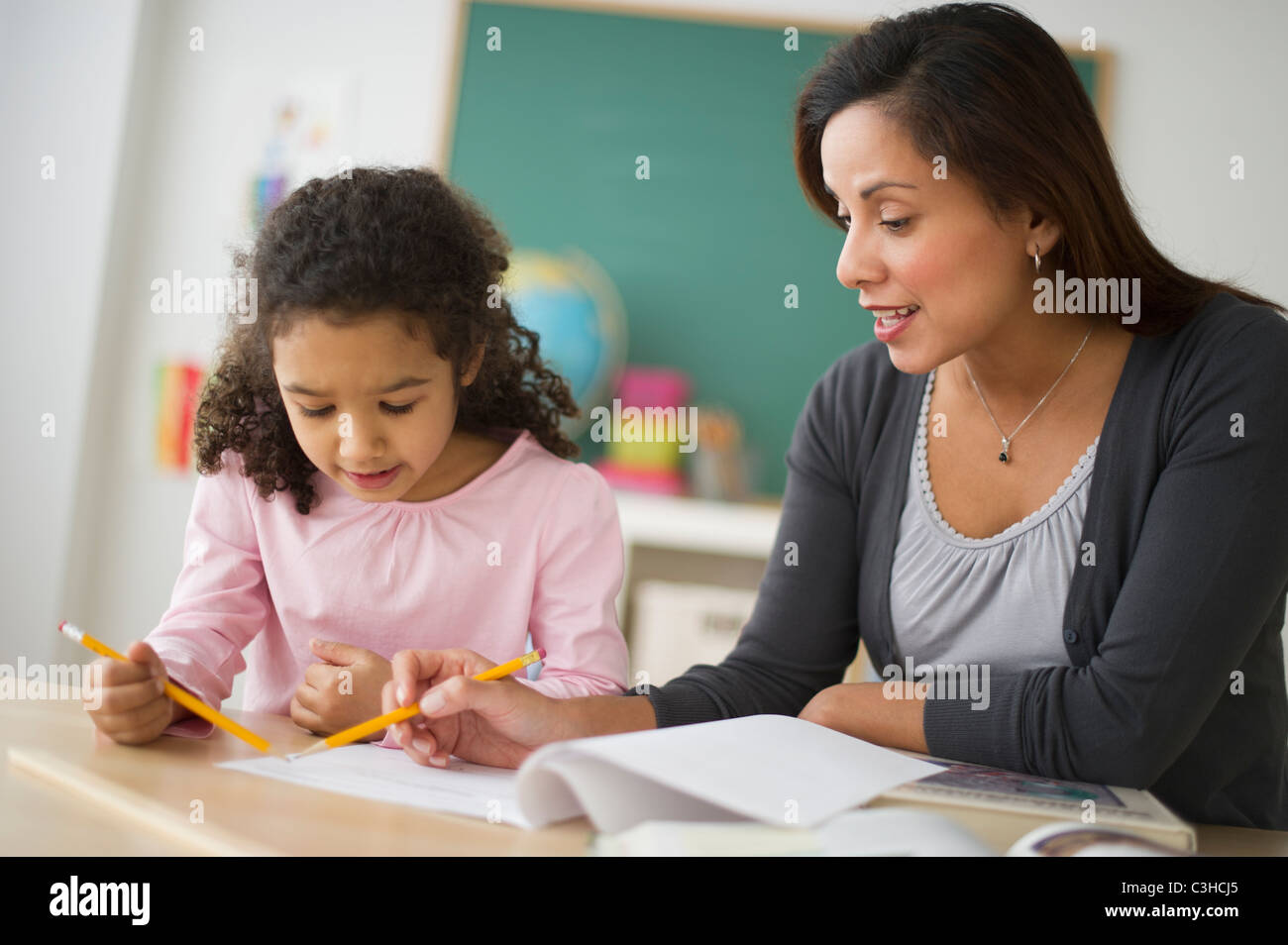 Girl (6-7) with female teacher sitting at desk in classroom Banque D'Images