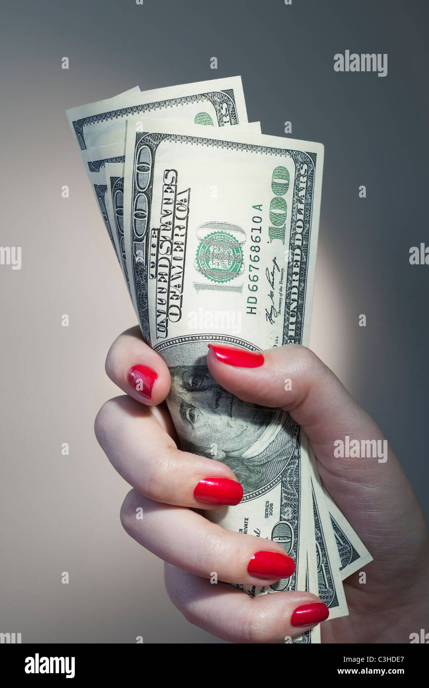 Close up of woman's hand holding vernis à ongles rouge avec bande de billets en dollars Banque D'Images