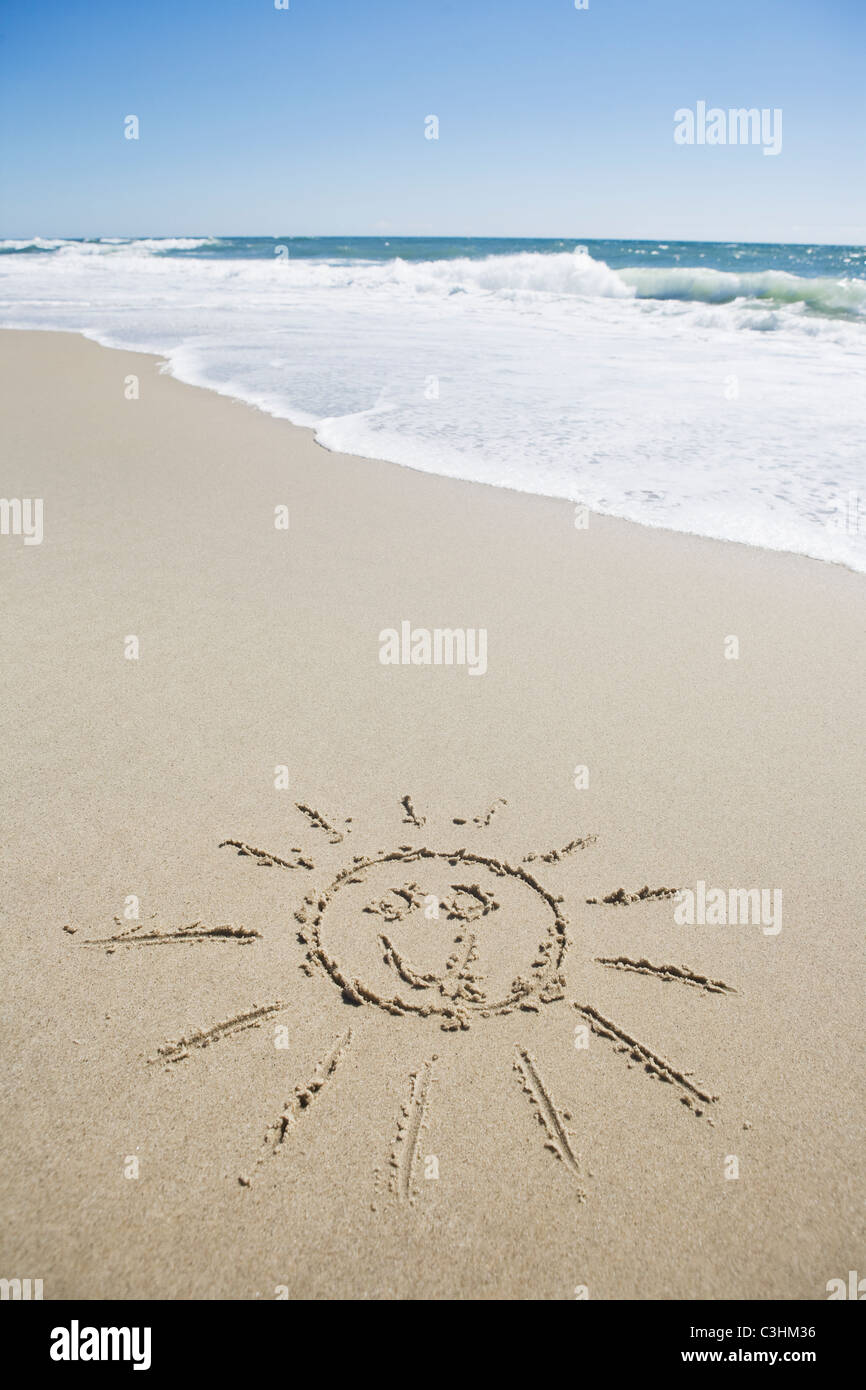 Visage soleil dessiné sur une plage de sable Banque D'Images
